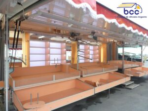 Camion marché textile panoramique avec chariots, étagères, cabines et enseigne motorisée. 12m de vente – Idéal lingerie et prêt-à-porter.