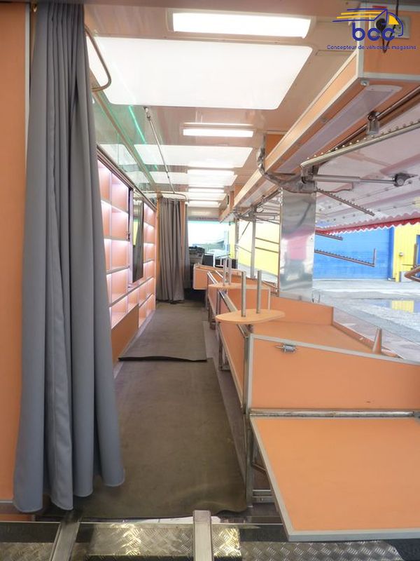 Camion marché textile panoramique avec chariots, étagères, cabines et enseigne motorisée. 12m de vente – Idéal lingerie et prêt-à-porter.